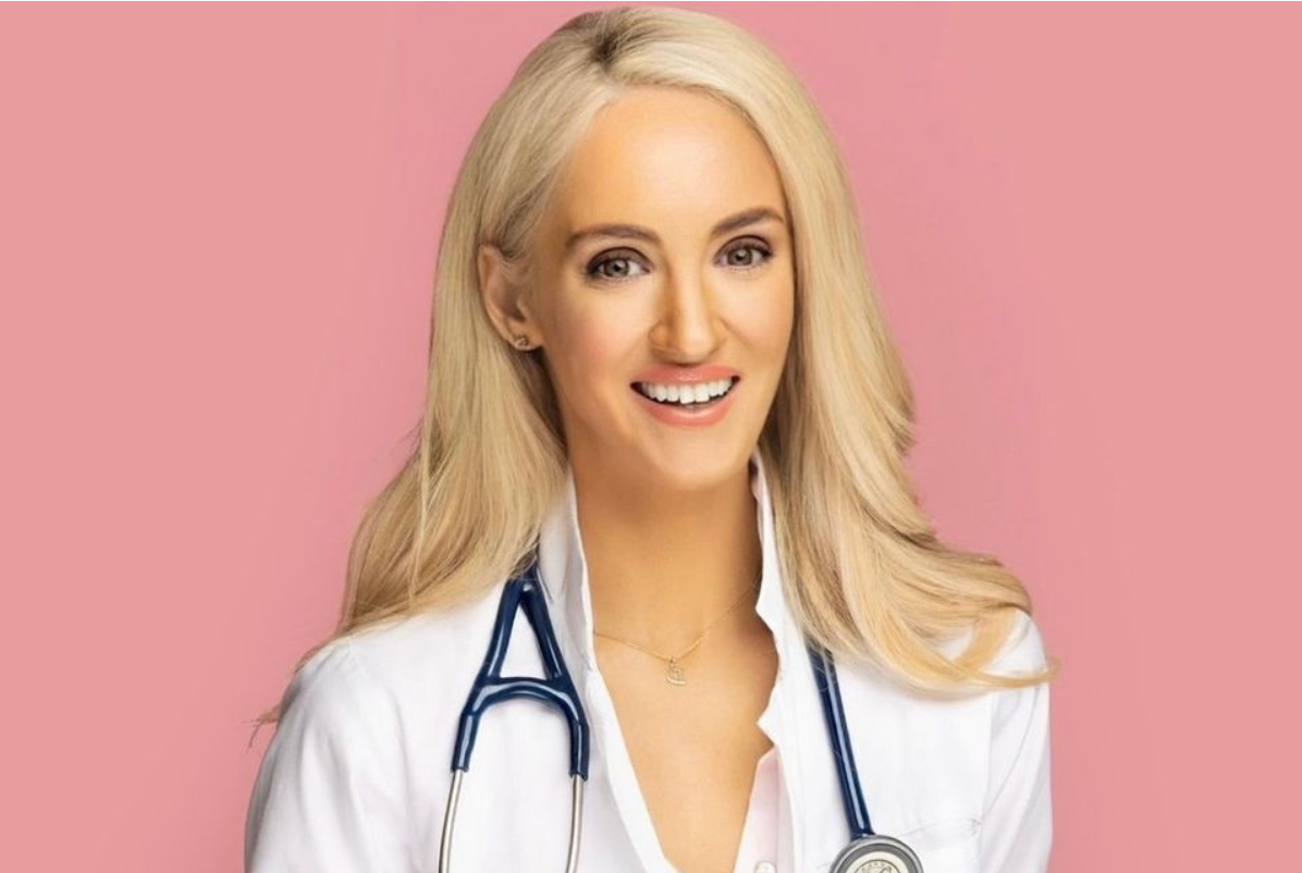Portrait of Dr. Doireann O’Leary smiling while wearing a white medical coat and stethoscope against a pink background. 